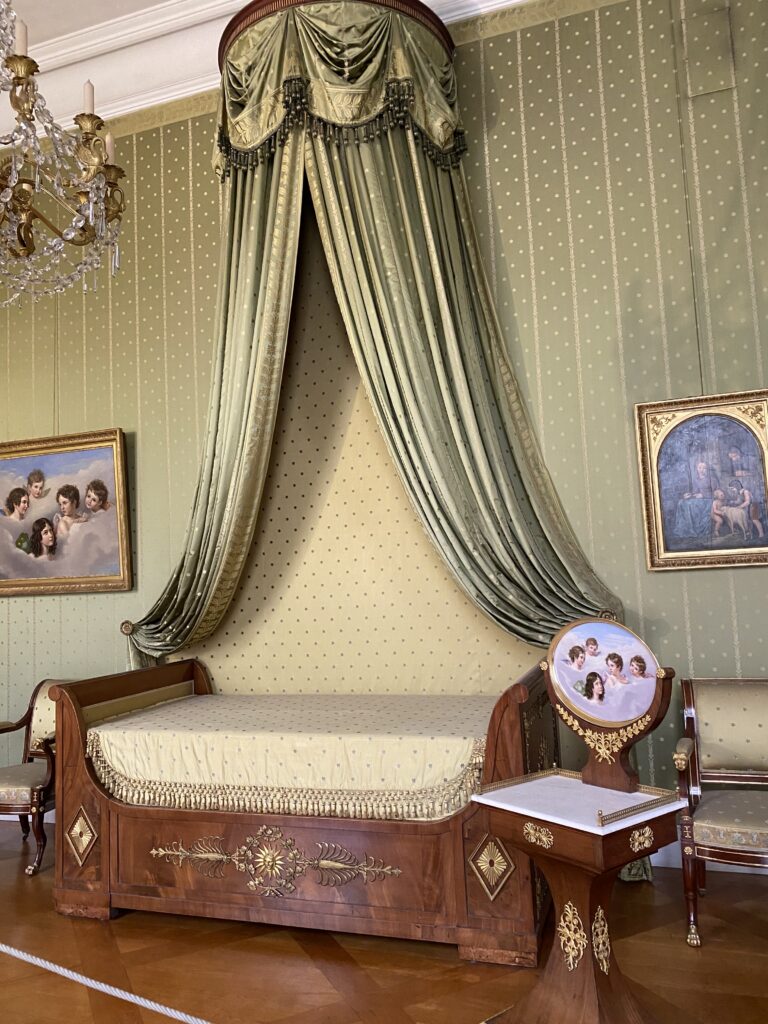 Bed in a museum with elegant curtains against a green patterned wall
