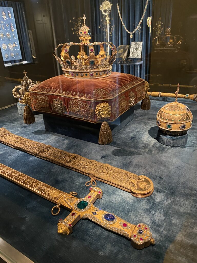 Museum display with a jeweled crown on a velvet pillow and a jeweled sword