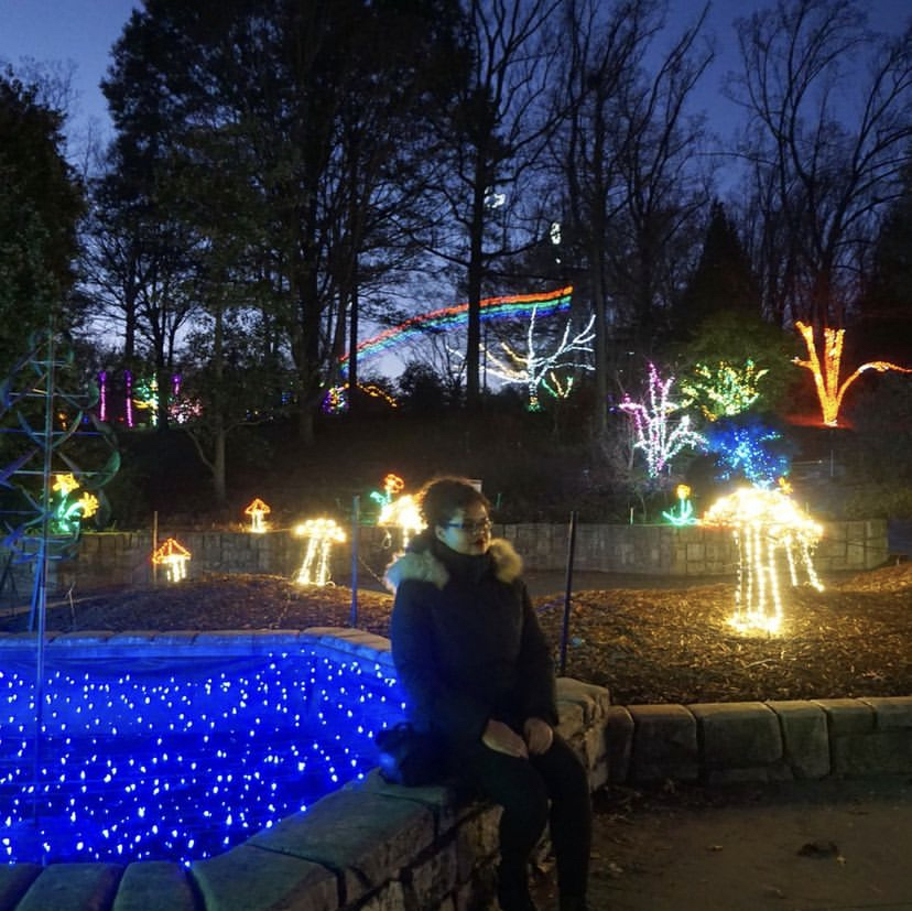 Woman sitting in garden at night among decorative Christmas lights 