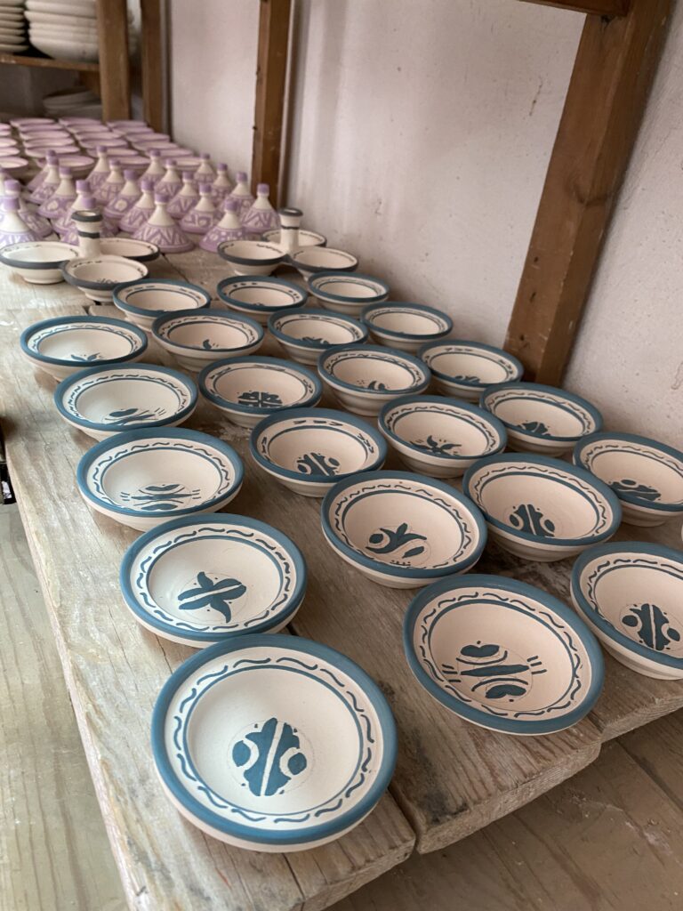 Three rows of painted clay dishes on a wooden shelf in a Fez pottery workshop