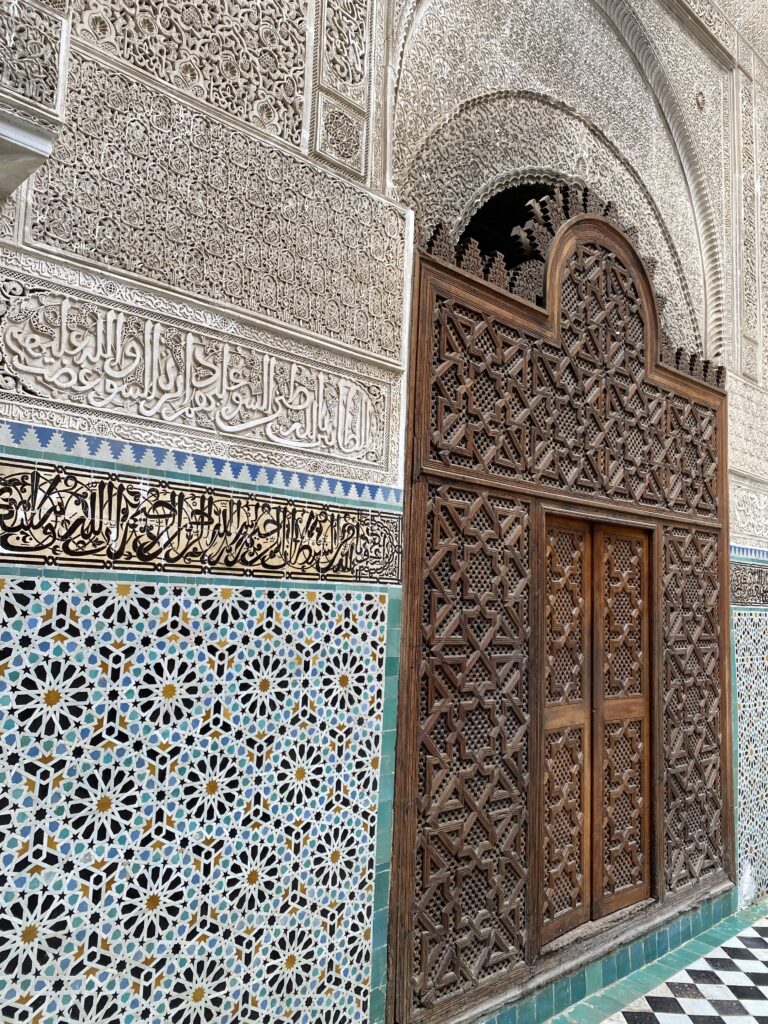 Tile and carving details on wall and wooden door in Fez Morocco historic madrasa