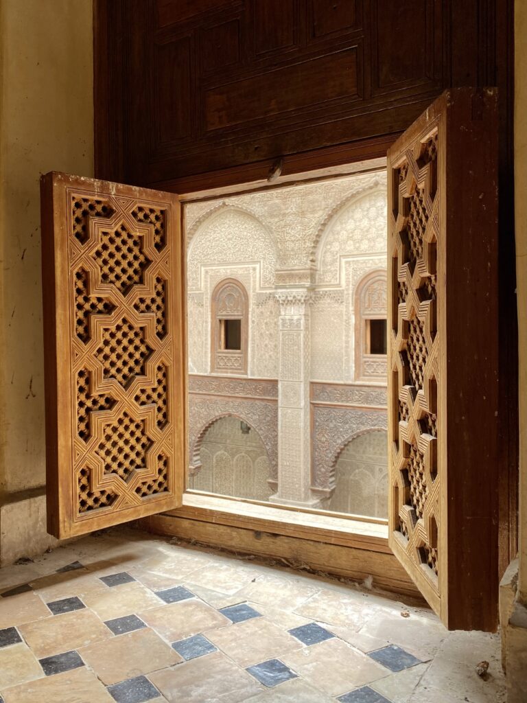 Wooden carved window looking out on historic madrasa courtyard in Fez Morocco