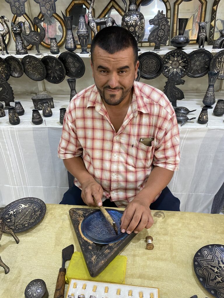 Moroccan artisan at his work station hammering silver thread into a metal plate