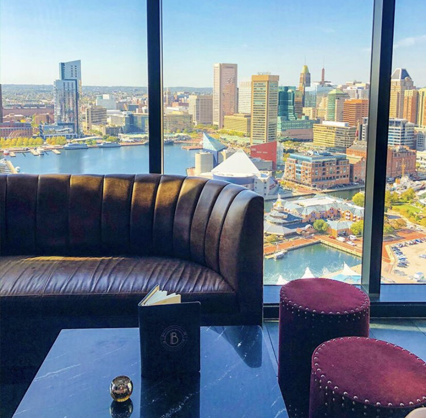 Brown sofa and lounge table in front of floor to ceiling windows with a view of Baltimore City