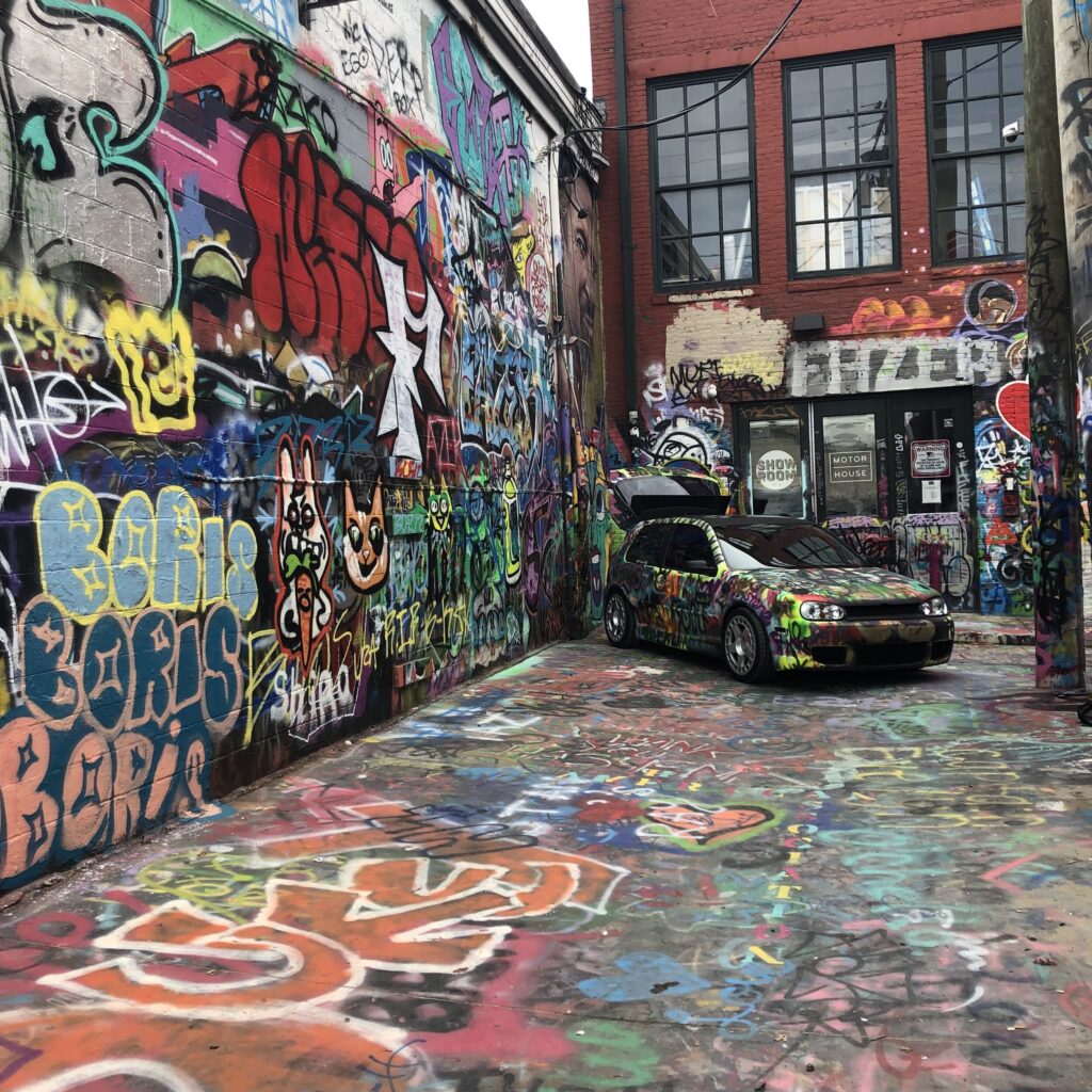 Alley covered in graffiti art and a small car parked there also covered in graffiti