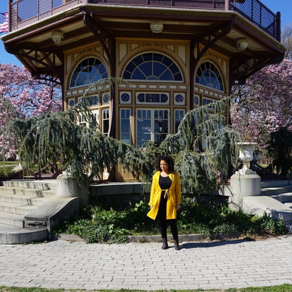 Woman in yellow jacket standing in front of Japanese-style park pagoda framed by magnolias