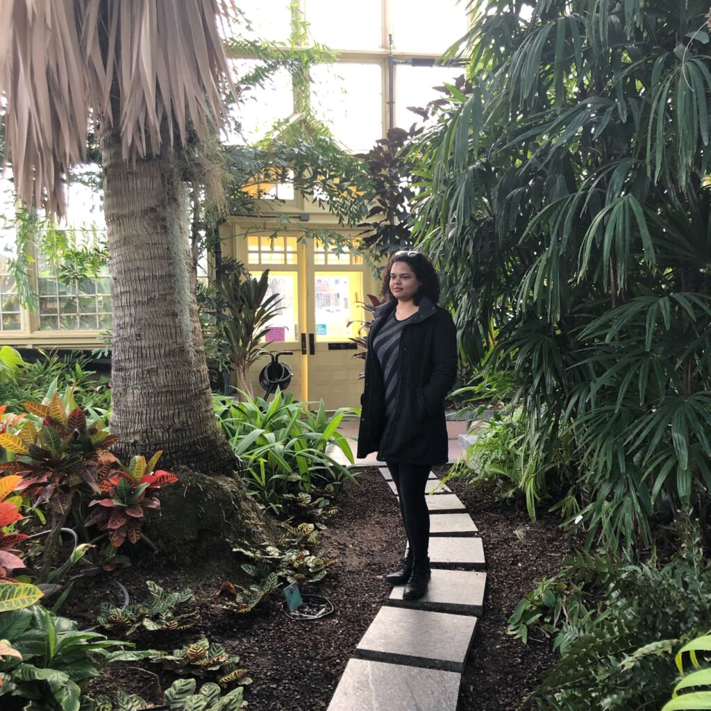 Woman standing on footpath between tropical plants and trees in a greenhouse