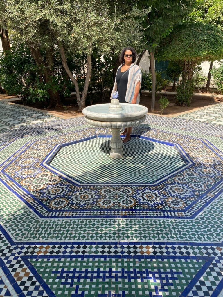 Woman standing in front of courtyard fountain with tile mosaic floors in Marrakesh Morocco palace
