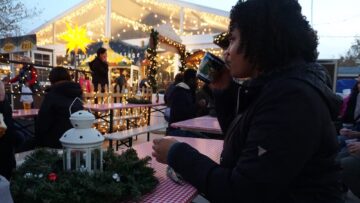 Woman sipping from a mug in a beer garden with Christmas lights