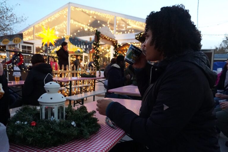 Woman sipping from a mug in a beer garden with Christmas lights