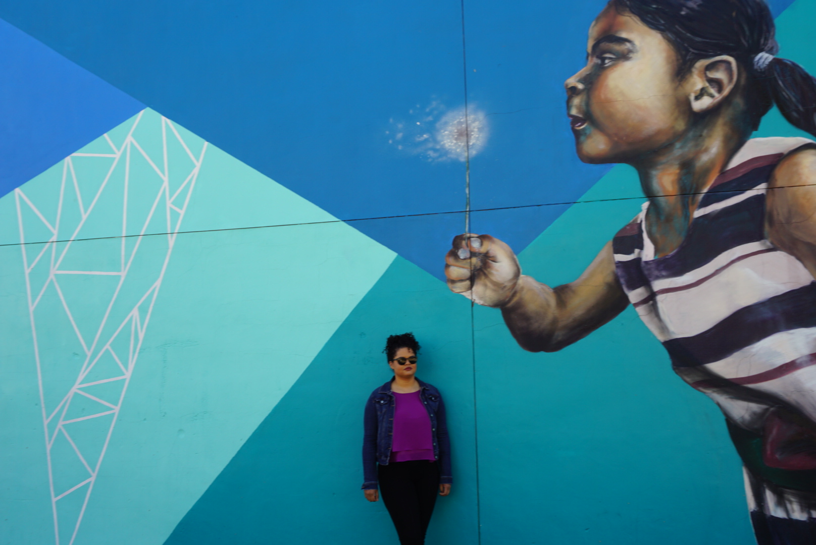 Woman standing in front of a large street mural of a little girl blowing a flower