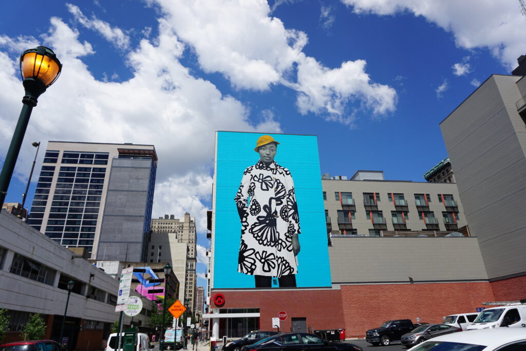 Colorful mural showing a woman in black and white coat on the side of a tall Philadelphia building