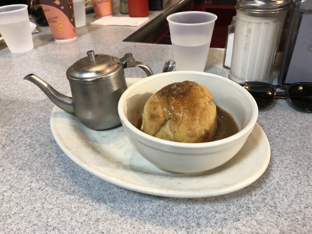 Plate holding an apple dumpling pastry in a bowl with a tin can of cream on the side