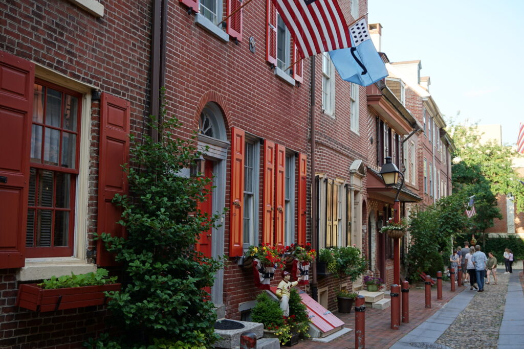 Colonial-style brick rowhomes with red shutters and greenery outside