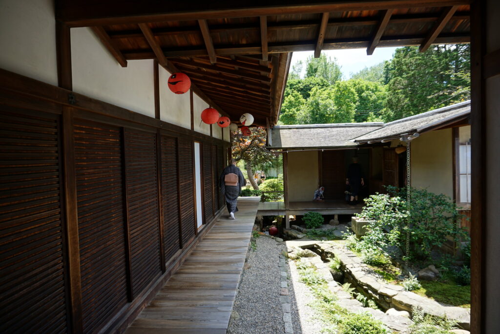 Japanese man in traditional clothing walking along a Japanese house and garden.