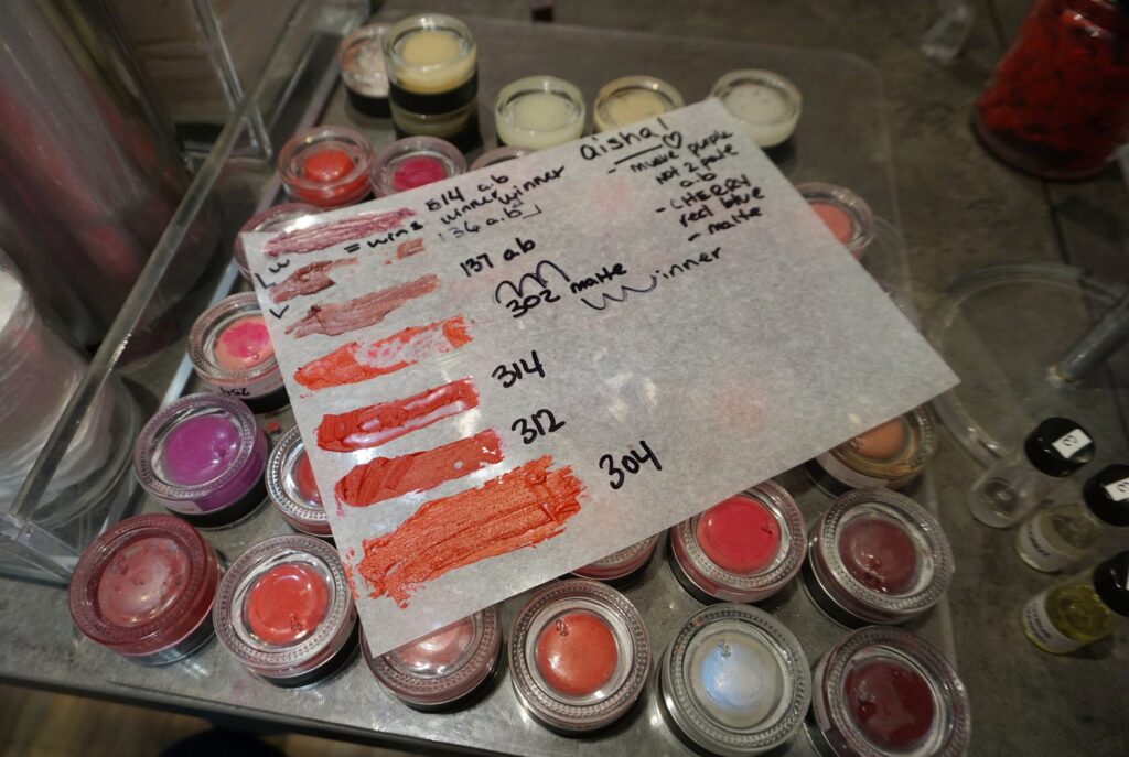 Small jars of lipstick pigments under a plastic sheet with color swatches