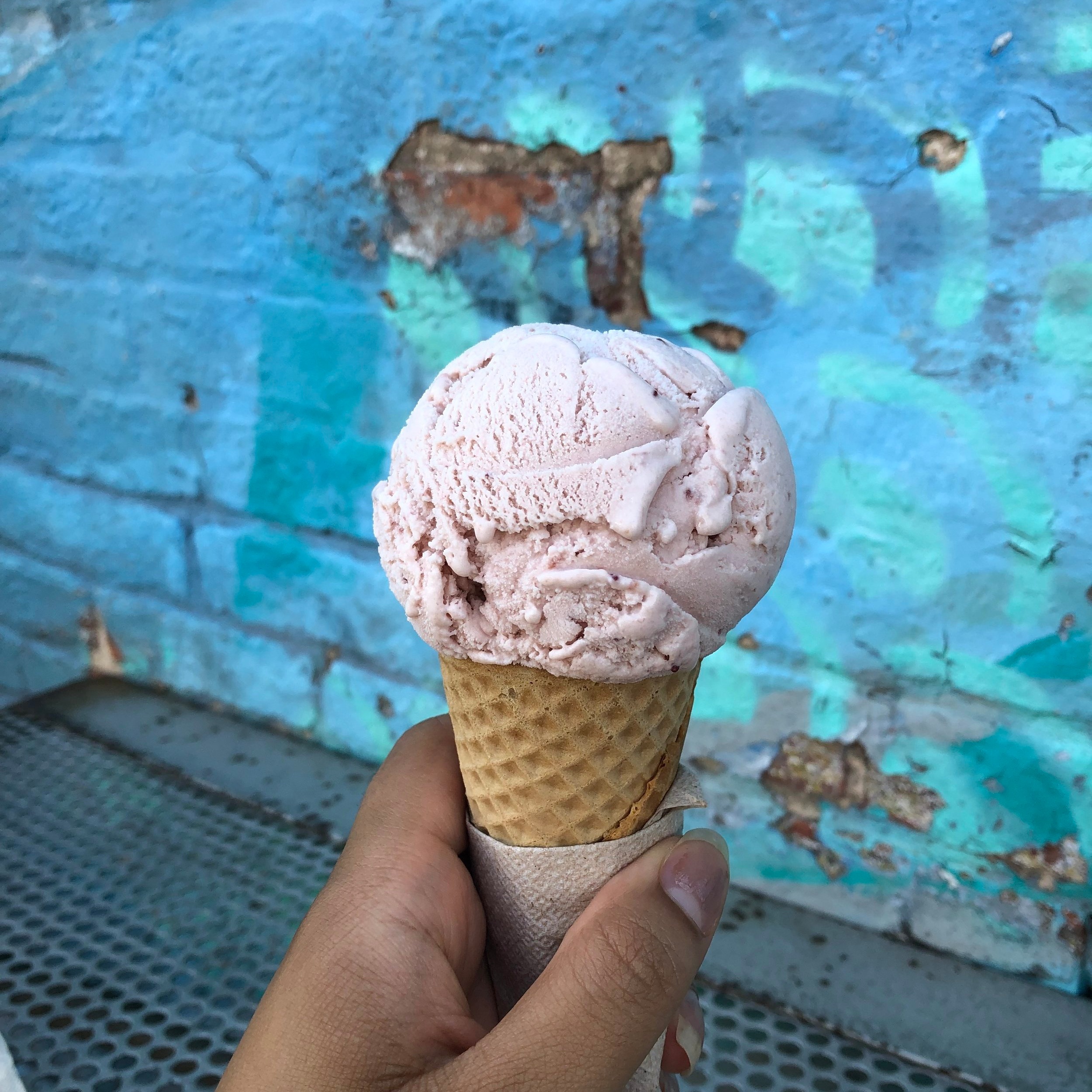 Hand holding a scoop of ice cream in a waffle cone in front of a blue brick wall on a summer's day in Baltimore Maryland.