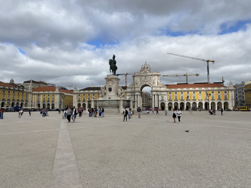 Large plaza with a statue in the center and surrounded by yellow buildings and a tall archway.