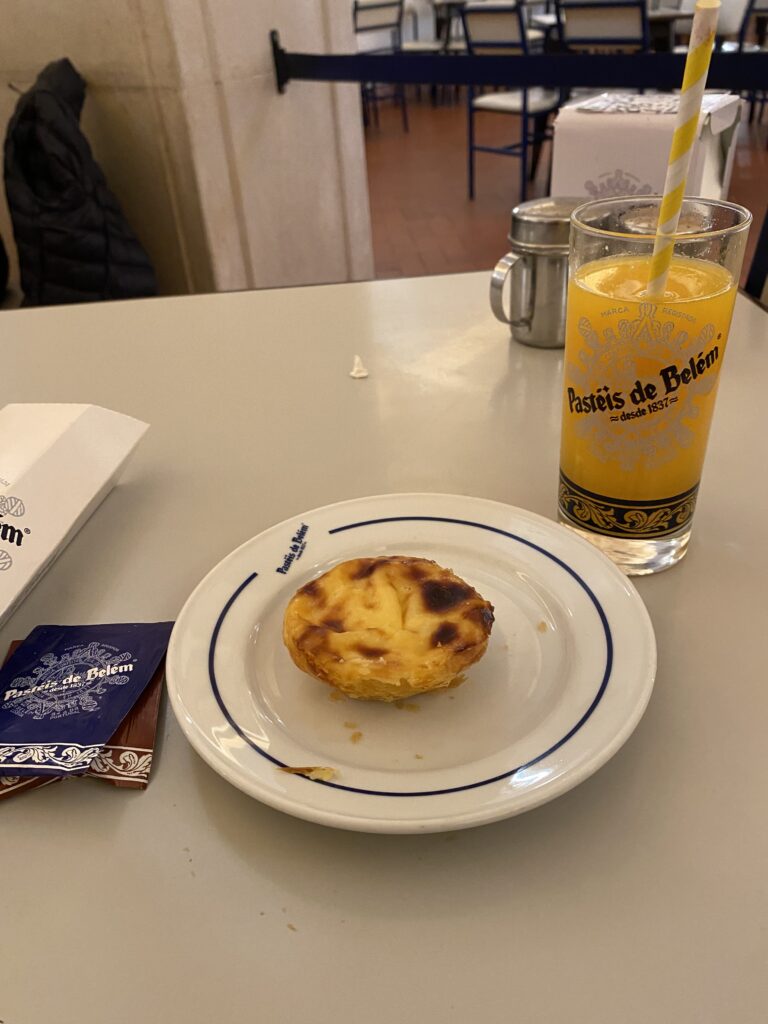 Plate holding a Portuguese custard pastry and glass of orange juice on a table.