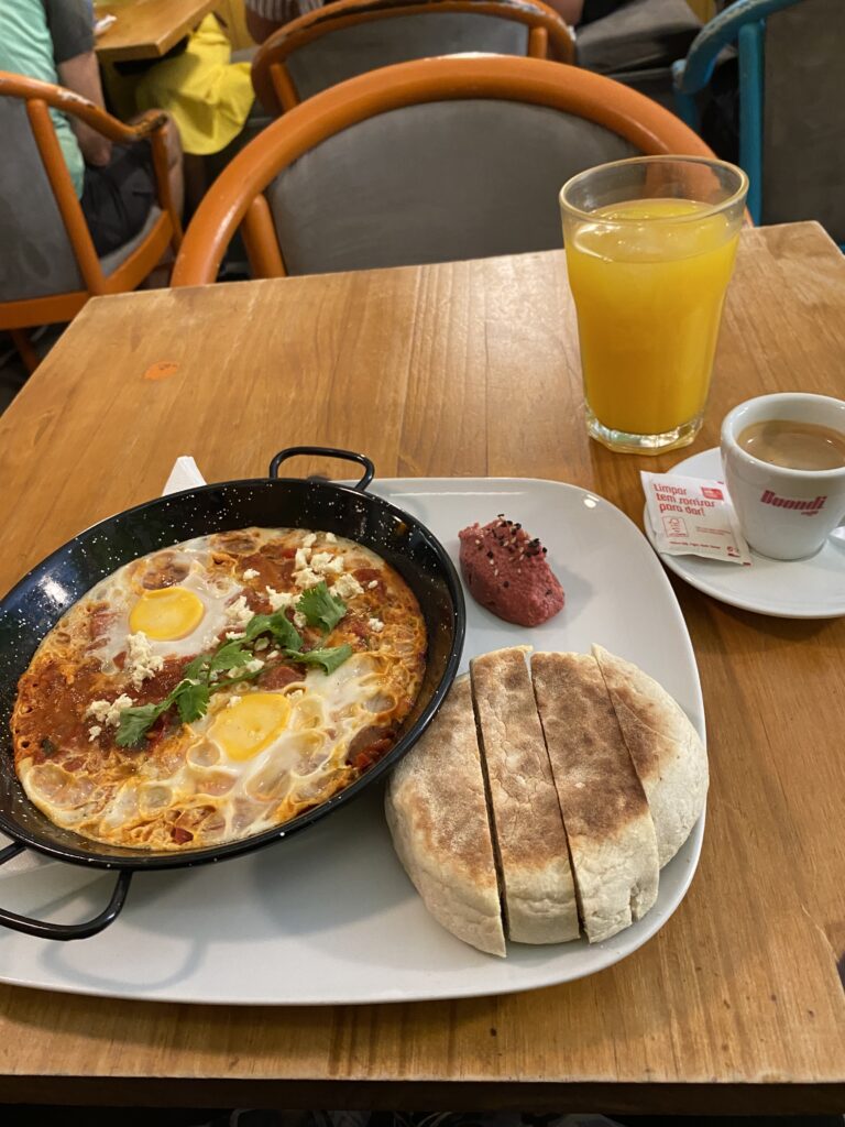 Plate of shakshuka and a bread roll and a glass of orange juice on a table.