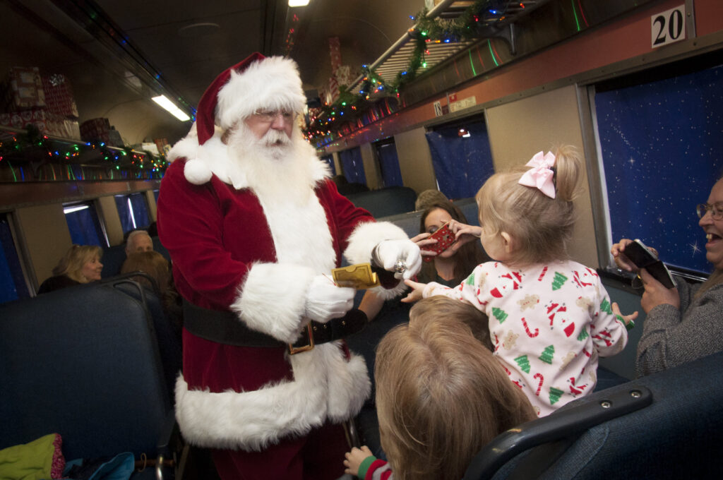 Man dressed as Santa Claus giving a golden ticket to a little girl on a train.