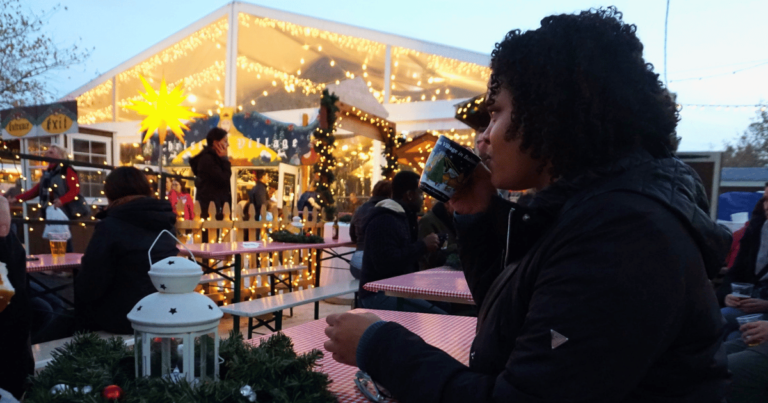 Woman sipping from a mug in a beer garden with Christmas lights