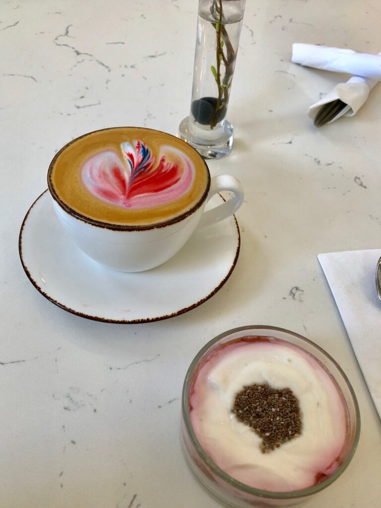 Mug of coffee with latte art and a bowl of yogurt on a cafe table.