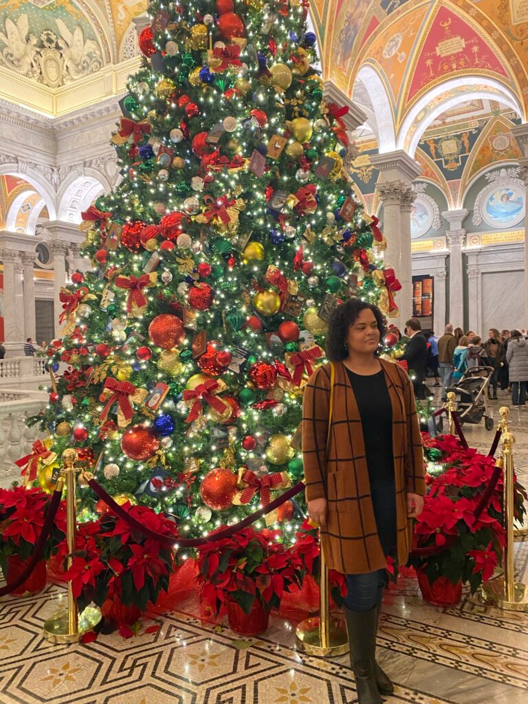 Woman standing in front of a tall 
Christmas tree in the lobby of the Library of Congress in Washington D.C.