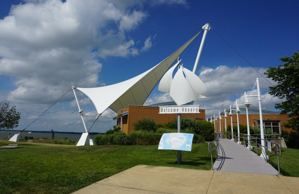 Building with decorative sails on it, a waterfront behind it, and blue sky with fluffy clouds