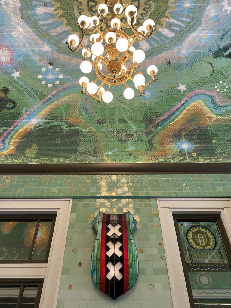 Detailed green and multicolored tiles on a wall and ceiling and a chandelier hanging from the ceiling