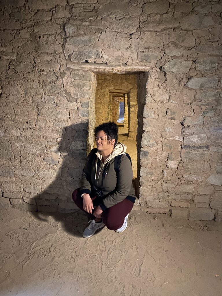 Woman crouching down in front of a series of door openings inside an Aztec ruins structure