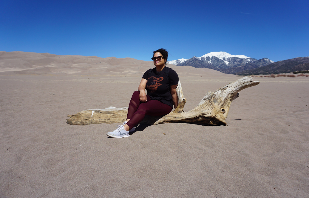 Woman sitting on log amid sand dunes during new mexico and southern colorado trip