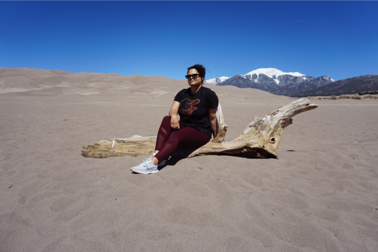 Woman sitting on log amid sand dunes during new mexico and southern colorado trip