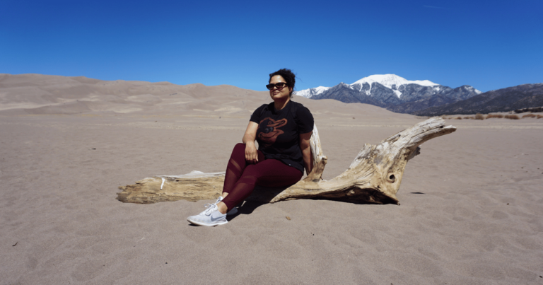 Woman sitting on log amid sand dunes during new mexico and southern colorado trip