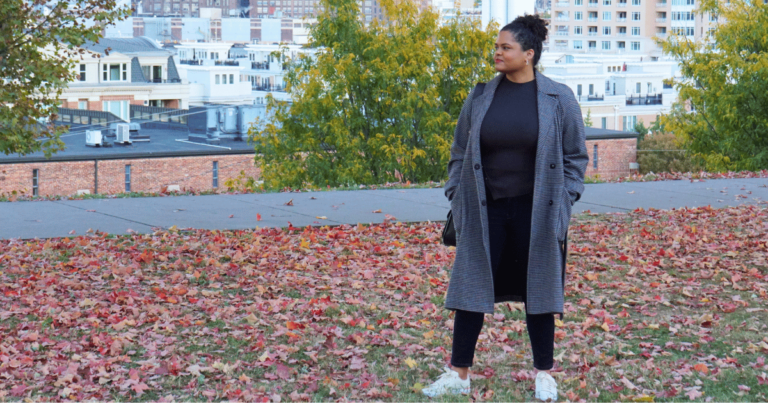 Woman in park overlooking a city with red and orange autumn leaves on the ground and trees with fall leaf colors