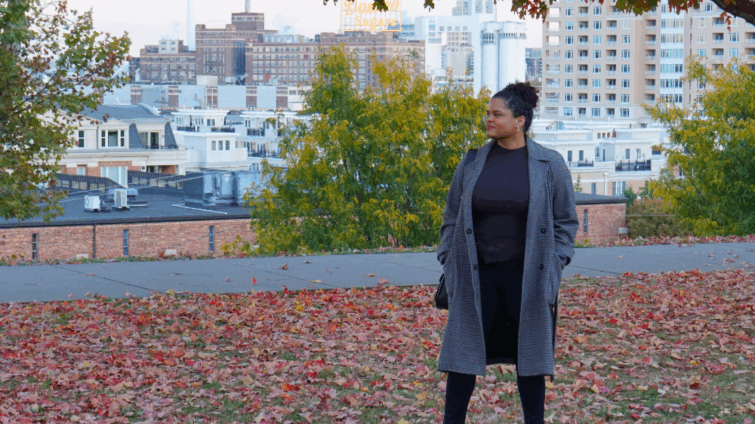 Woman in park overlooking a city with red and orange autumn leaves on the ground and trees with fall leaf colors