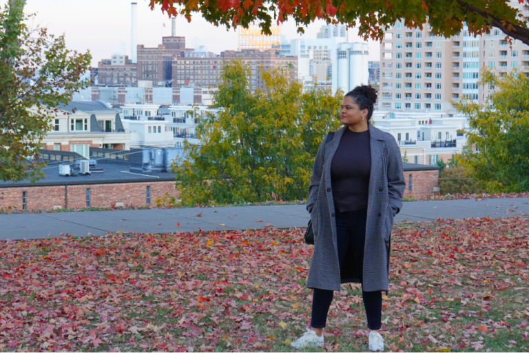 Woman in park overlooking a city with red and orange autumn leaves on the ground and trees with fall leaf colors