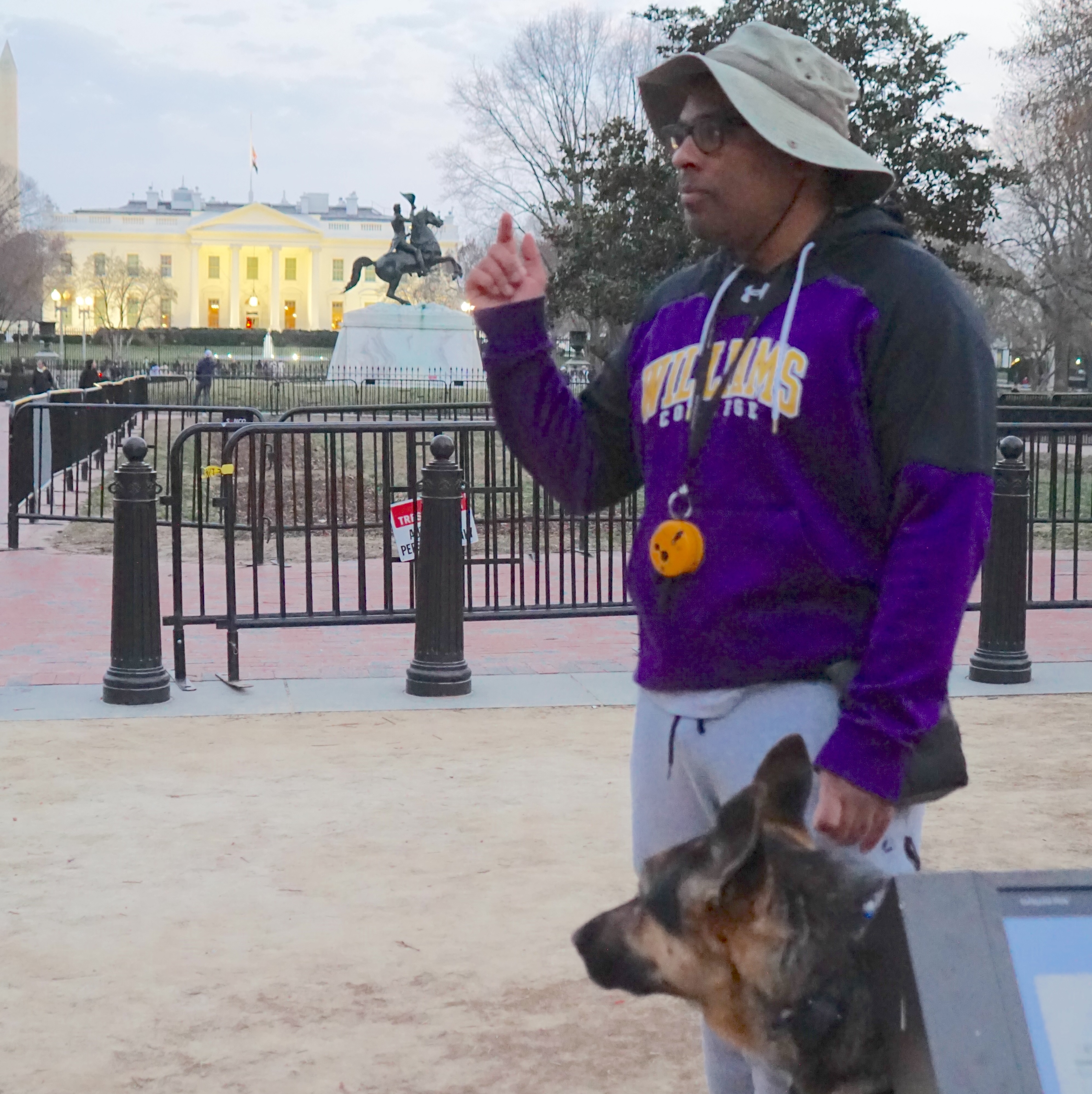 Man speaking and holding dog on leash with the White House in the background