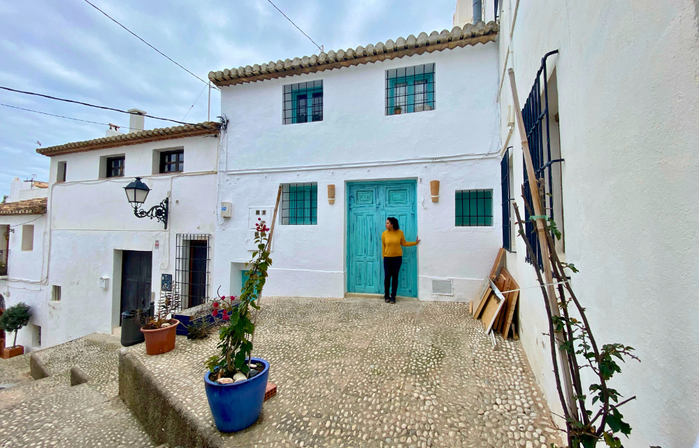 Woman standing in front of the blue green door of a row of white houses in a Spanish beach town
