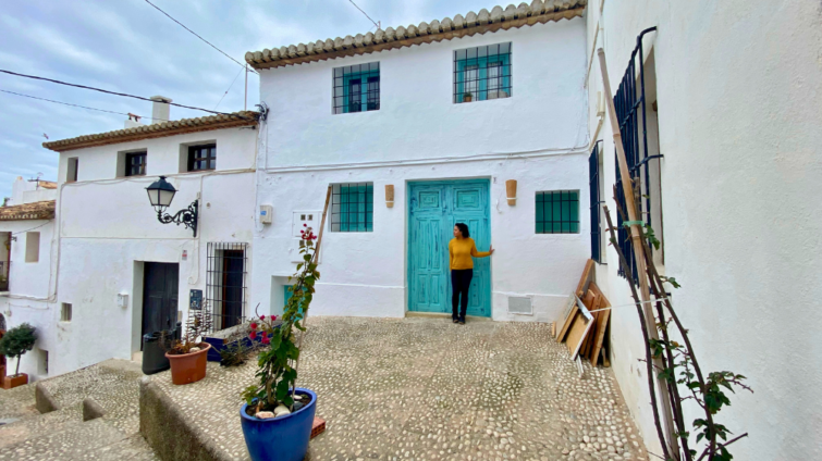 Woman standing in front of the blue green door of a row of white houses in a Spanish beach town