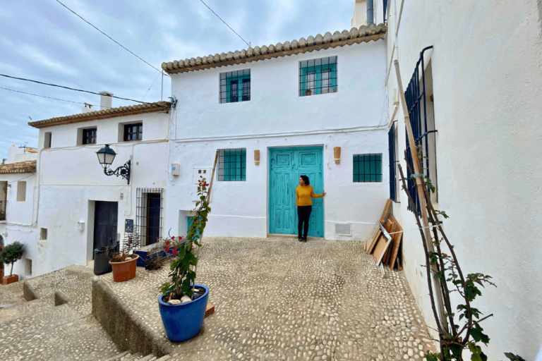 Woman standing in front of the blue green door of a row of white houses in a Spanish beach town