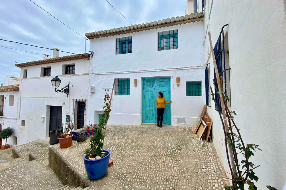 Woman standing in front of the blue green door of a row of white houses in a Spanish beach town