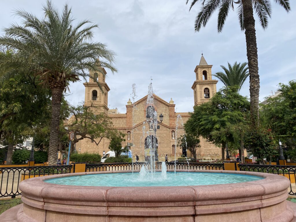 Old church surrounded by palm trees with a round fountain in the foreground