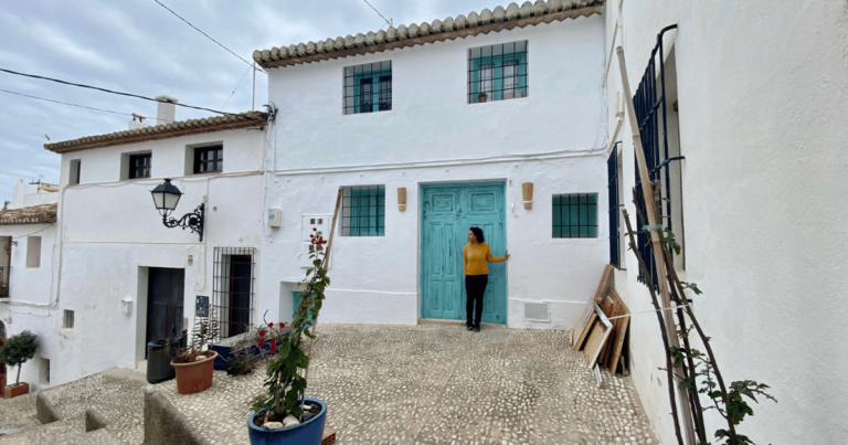 Woman standing in front of the blue green door of a row of white houses in a Spanish beach town
