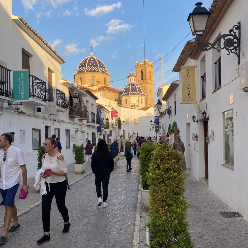 Cobblestone street lined with shops and a domed church in the distance