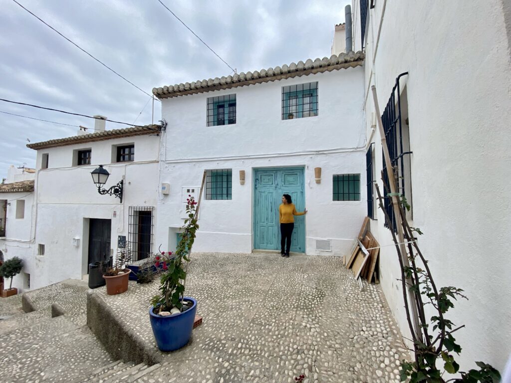 Woman standing in front of the blue green door of a row of white houses in a Spanish Mediterranean beach town