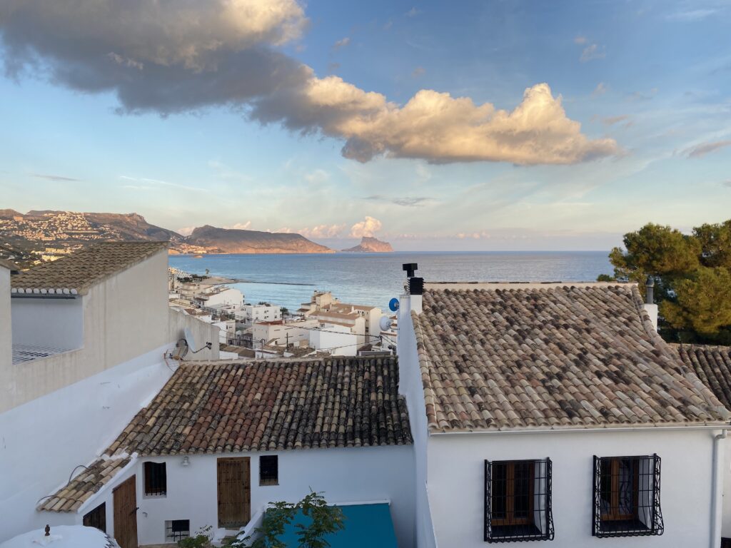 View of the Mediterranean Sea and blue sky beyond a row of white houses with Mediterranean-tiled roofs