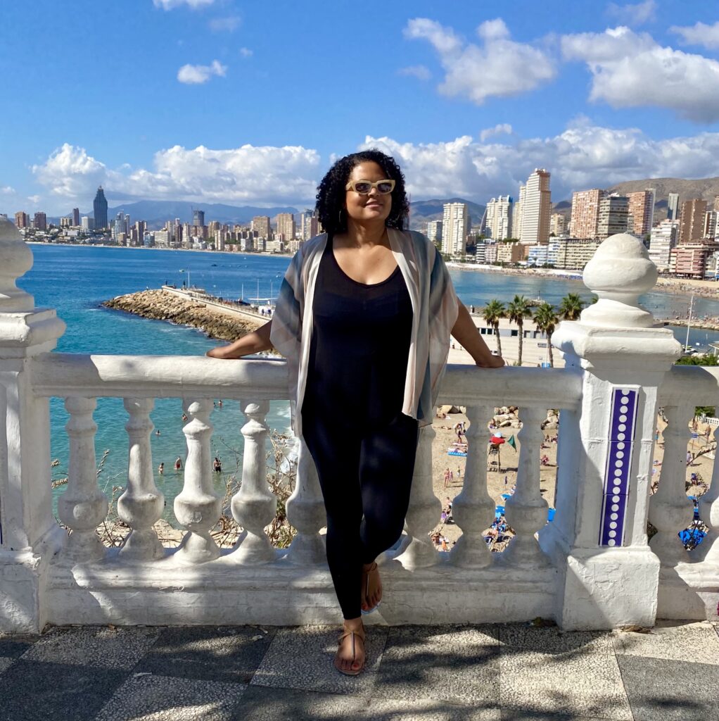 Smiling woman posing in front of white balcony fence with Benidorm Spain beach in background