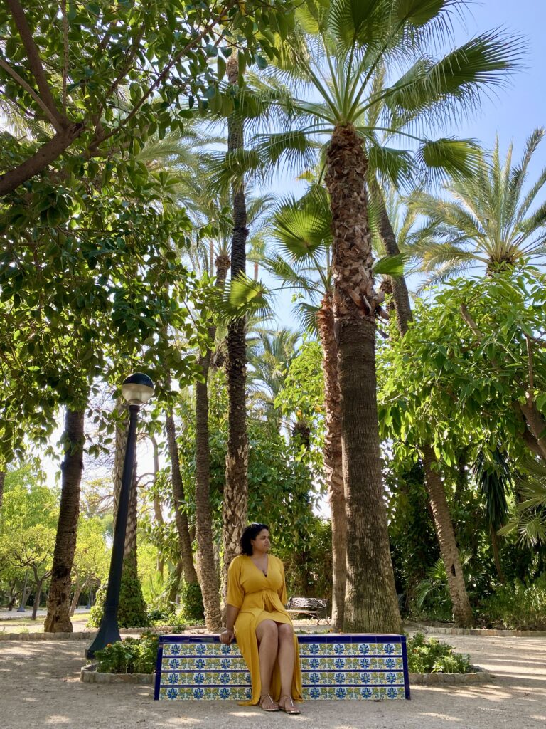 Woman in yellow dress sitting on a tiled bench with tall palm trees all around