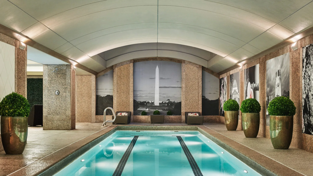 Indoor lap pool lined with potted plants, arched ceiling, and image of the Washington Monument on the wall